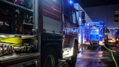 Rotes Feuerwehrfahrzeug mit offenen Abteilen und gelben Schläuchen bei Nacht