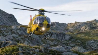 Gelber Rettungshubschrauber fliegt über felsigem Berggelände mit grünen Flächen