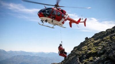 Roter Rettungshubschrauber schwebt über einem felsigen Berggrat und lässt einen Retter ab