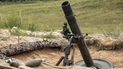 Aufgestellter Granatwerfer mit Munition auf Tarnnetz in einer Wiese