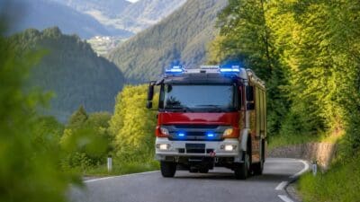 Rotes Feuerwehrfahrzeug mit blauem Blaulicht auf einer kurvigen Straße in den Bergen