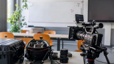 Professionelle Filmkamera auf Stativ mit Objektiven und Taschen in einem Klassenzimmer