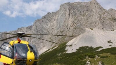Gelber Rettungshubschrauber mit offener Tür vor steiler Felswand auf der Rax