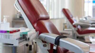 Rote Blutspende-Liegen mit Tablett voller Blutprobenröhrchen in einem hellen Behandlungsraum