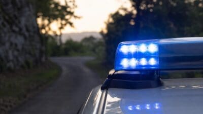 Blaues Blaulicht eines Polizeifahrzeugs auf einer kurvigen Landstraße bei Dämmerung