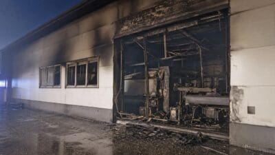 Nachtaufnahme eines brandgeschädigten Firmengebäudes mit zerstörten Fenstern und offener Halle mit zerstörter Maschine