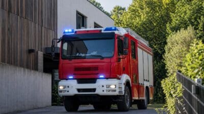 Rotes Feuerwehrfahrzeug mit blauem Blaulicht vor einem Gebäude mit Holzfassade