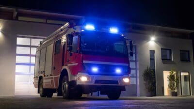 Rotes Feuerwehrfahrzeug mit eingeschalteten Blaulichtern vor einem Gebäude bei Nacht