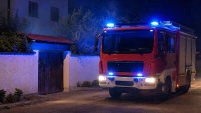 Rotes Feuerwehrfahrzeug mit blauem Blaulicht vor einer weißen Mauer bei Nacht