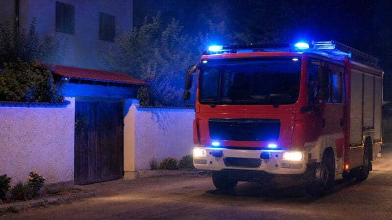 Rotes Feuerwehrfahrzeug mit blauem Blaulicht vor einer weißen Mauer bei Nacht
