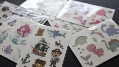 Mehrere Bögen mit bunten Klebetattoos für Kinder zeigen Piraten, Dinosaurier, Haie und Meerjungfrauen.