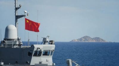 Chinesisches Kriegsschiff mit wehender Nationalflagge auf dem Meer vor einer Insel
