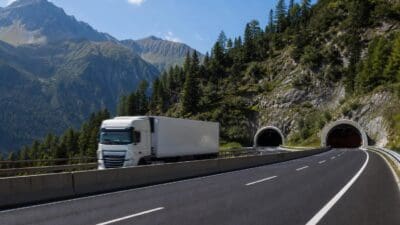 Weißer Lastwagen fährt auf einer kurvigen Straße auf zwei Tunnel in den Bergen zu