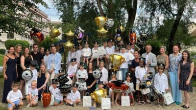 Gruppe von Kindergartenkindern in Abschlusskleidung mit Luftballons und Erwachsenen bei einer Feier im Freien