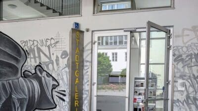 Eingang der Stadtgalerie Klagenfurt mit offenen Glastüren und Graffiti an den Wänden