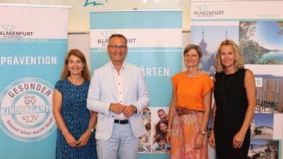Vier Erwachsene stehen vor Werbebannern der Stadt Klagenfurt zu Kindergärten und Prävention.