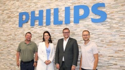 Vier Personen stehen vor einer Steinwand mit dem großen blauen Philips-Logo.