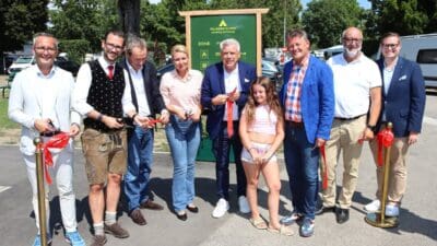 Mehrere Personen in formeller und traditioneller Kleidung bei der Banddurchschneidung vor dem Schild des Falkensteiner Camping Wörthersee.