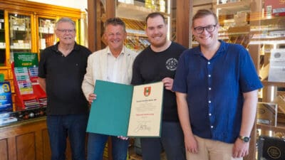 Vier Männer stehen in einer Trafik und präsentieren eine geöffnete Dankesurkunde.