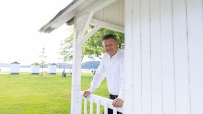 Bürgermeister Christian Scheider lehnt an der weißen Holzveranda eines Gebäudes im Strandbad Klagenfurt.