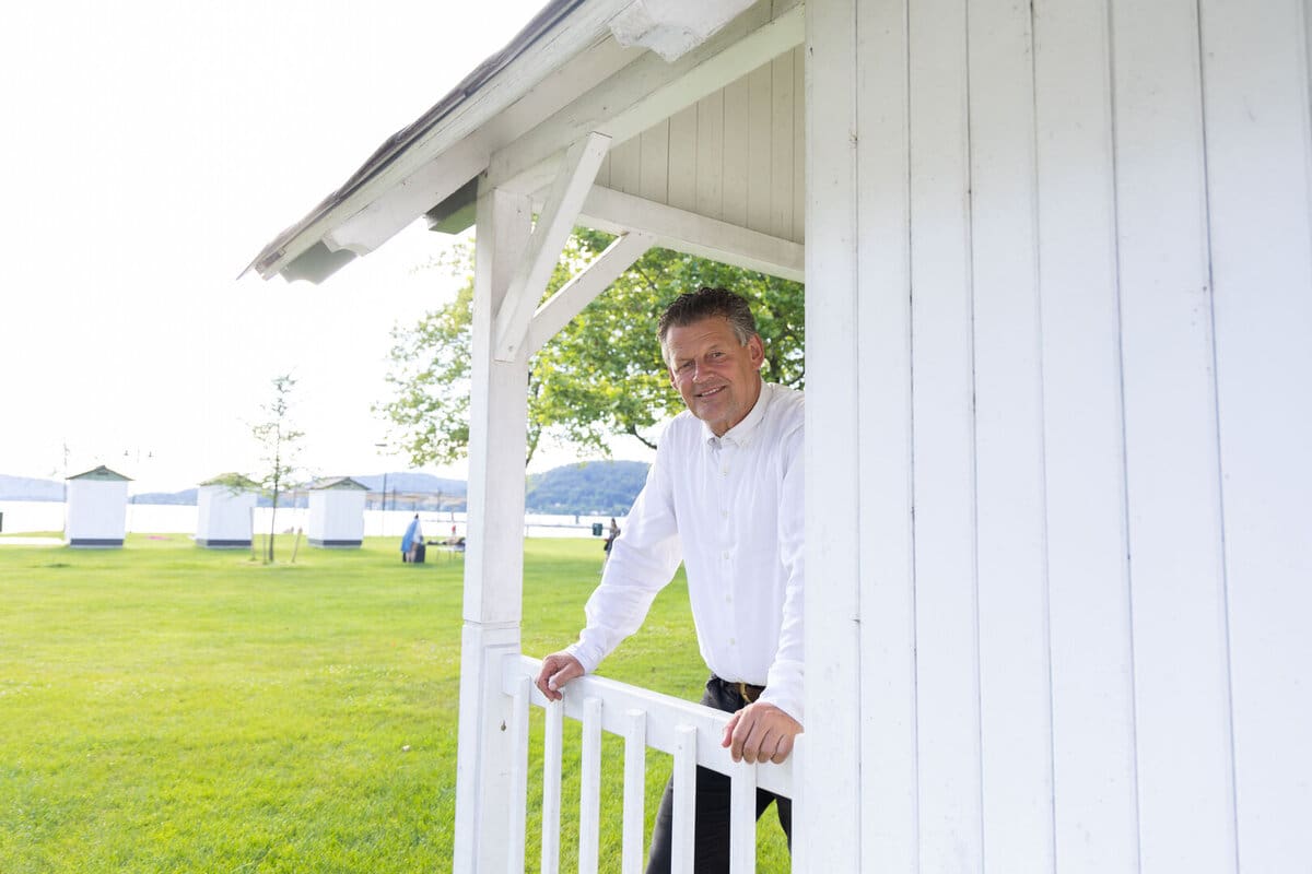 Bürgermeister Christian Scheider lehnt an der weißen Holzveranda eines Gebäudes im Strandbad Klagenfurt.