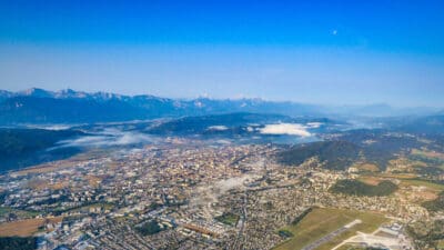 Luftaufnahme von Klagenfurt mit dem Wörthersee, dem Flughafen und den umliegenden Bergen unter klarem Himmel.
