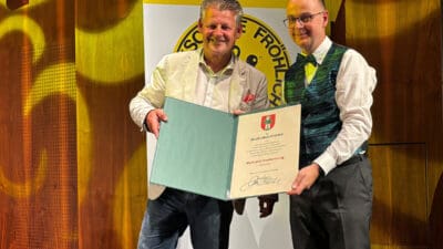 Zwei Männer präsentieren eine geöffnete Mappe mit Urkunde der Musikschule Fröhlich.
