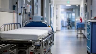 Leeres Krankenhausbett mit Infusionsständer in einem hellen Krankenhausflur