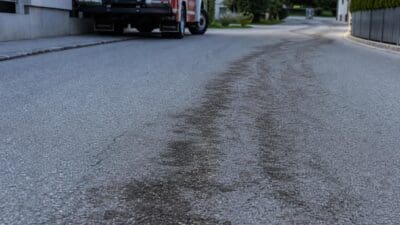 Dunkle Ölspur auf der Straße mit Feuerwehrfahrzeug im Hintergrund