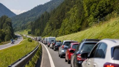 Lange Kolonne von Autos und Lastwagen im Stau auf einer Straße zwischen grünen Bergen und Wäldern