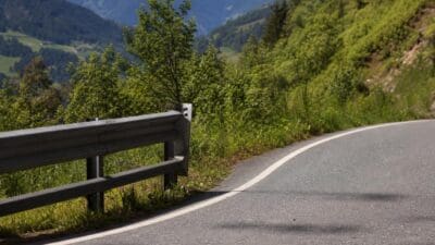Gekrümmte Asphaltstraße mit grauer Leitplanke am Rand in bergiger Landschaft