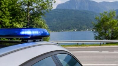 Blaues Blaulicht auf dem Dach eines Polizeifahrzeugs vor einem See und Bergen