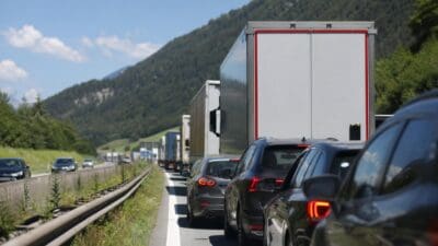 Mehrere Autos und Lastwagen stehen im Stau auf der Autobahn mit grünen Bergen im Hintergrund