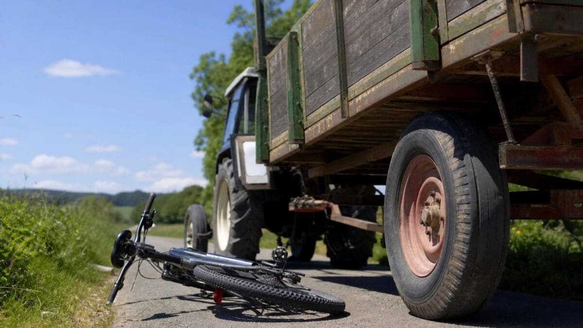 Ein umgestürztes E-Bike liegt auf einer Landstraße neben einem Traktor mit Anhänger.