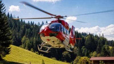 Roter und weißer Rettungshubschrauber mit rotem Kreuz fliegt über grünen Hügeln