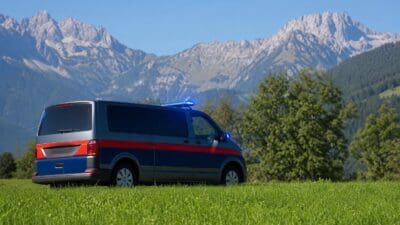 Polizeiwagen mit Blaulicht parkt auf grüner Wiese vor schneebedeckten Bergen