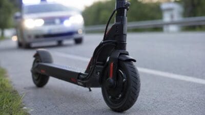 Ein schwarzer E-Scooter steht am Straßenrand vor einem Polizeiauto mit Blaulicht