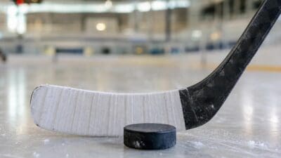 Nahaufnahme eines Eishockeyschlägers mit weißem Tape und einem Puck auf dem Eis