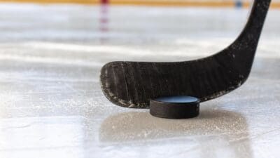 Ein schwarzer Eishockeyschläger berührt einen Puck auf dem Eis