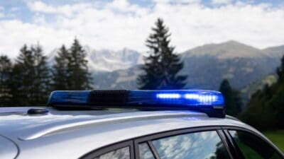 Blaues Blaulicht auf dem Dach eines silbernen Polizeifahrzeugs vor Berglandschaft