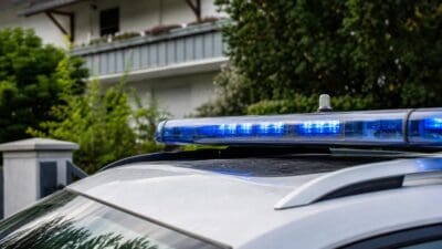 Blaues Blaulicht eines Polizeifahrzeugs leuchtet vor einem Wohnhaus mit Balkon.