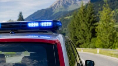 Blaulicht leuchtet auf dem Dach eines roten und silbernen Polizeifahrzeugs vor Berglandschaft.