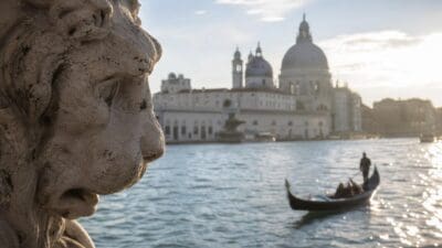 Steinerner Löwenkopf im Vordergrund mit Gondel auf dem Wasser und Basilika im Hintergrund in Venedig