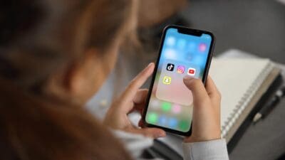 Eine Frau hält ein Smartphone mit Apps von TikTok, Instagram, YouTube und Snapchat.