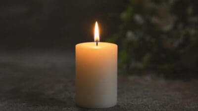 Brennende weiße Stumpenkerze auf dunkler Oberfläche vor unscharfem Hintergrund