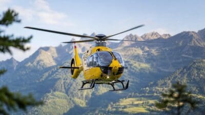 Gelber Rettungshubschrauber fliegt über grüne Berge und Täler.