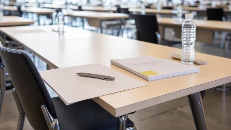 Ein leerer Tisch mit Stift, Papier, Mappe und Wasserflasche in einem großen Prüfungssaal.