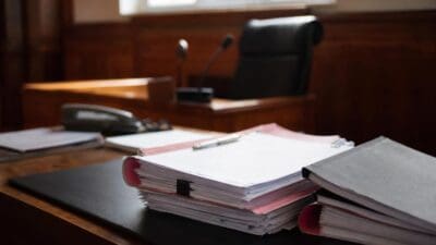 Aktenordner und Stapel mit Papieren auf einem Holztisch im Gerichtssaal