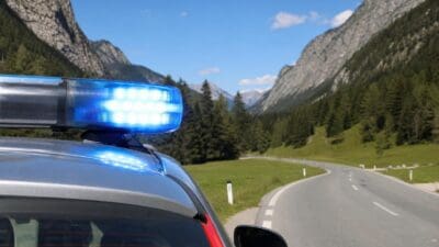 Blaues Blaulicht eines Einsatzfahrzeugs auf dem Dach vor einer Berglandschaft mit kurviger Straße