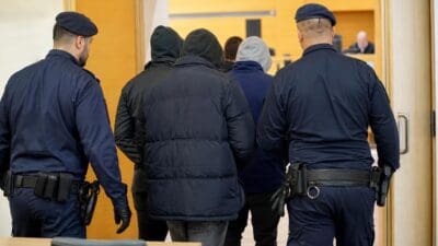 Polizisten führen mehrere vermummte Personen durch eine Tür in einen Saal